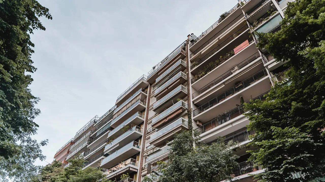 Prédio residencial de vários andares visto de baixo, entre árvores; imagem ilustrativa