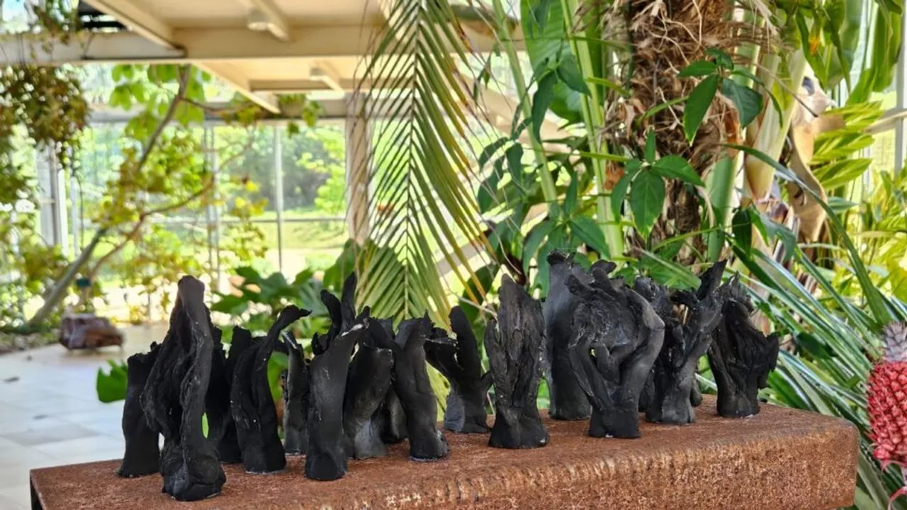 Esculturas de cerâmica escura sobre uma base marrom, cercadas por plantas no Palacete de Cristal