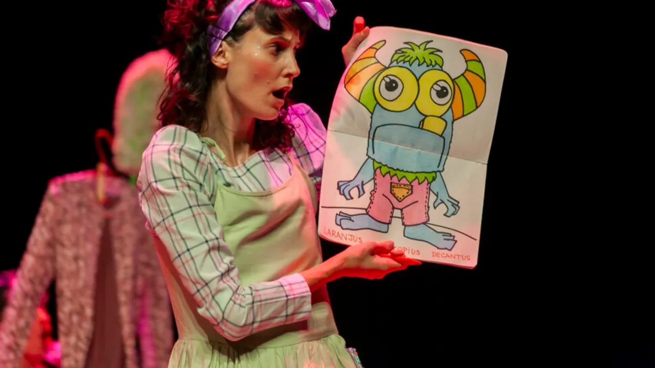 Atriz em cena segura cartaz com desenho colorido durante apresentação infantil