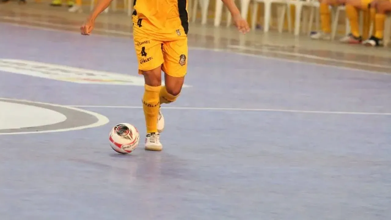 Bola de futsal e pernas de jogador em quadra de ginásio