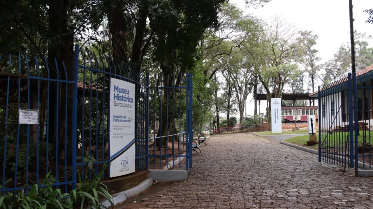 Entrada do Museu Histórico Sorocabano com portões azuis, caminho de paralelepípedos e árvores