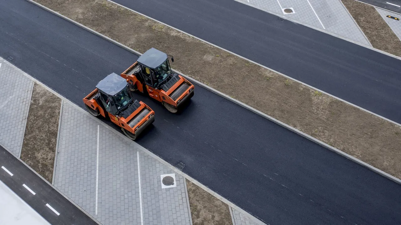 Vista aérea de rolo compactador laranja sobre asfalto novo em obra de pavimentação; imagem ilustrativa