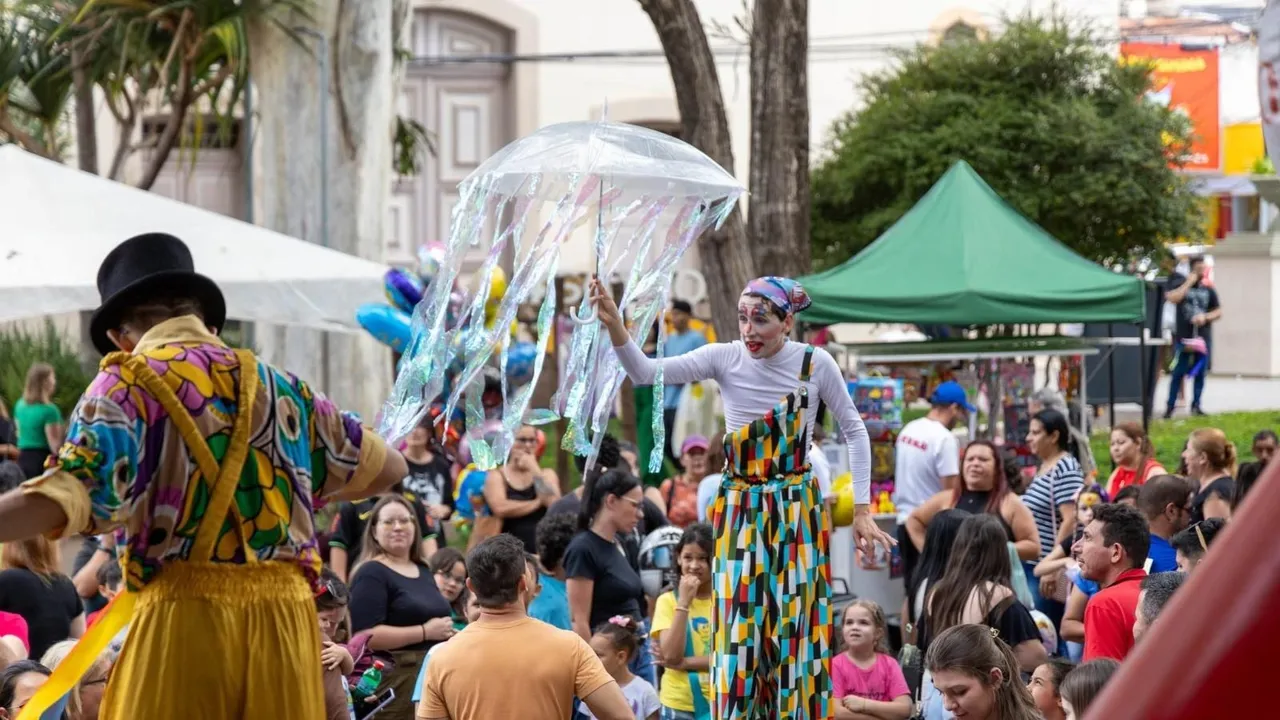 Artistas em pernas de pau se apresentam para crianças e famílias em uma praça arborizada
